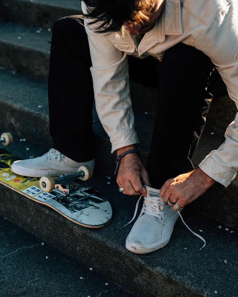 Skateboarder lacing up white skate shoes while sitting on steps with board beside them—shop our skateboard shoes collection.