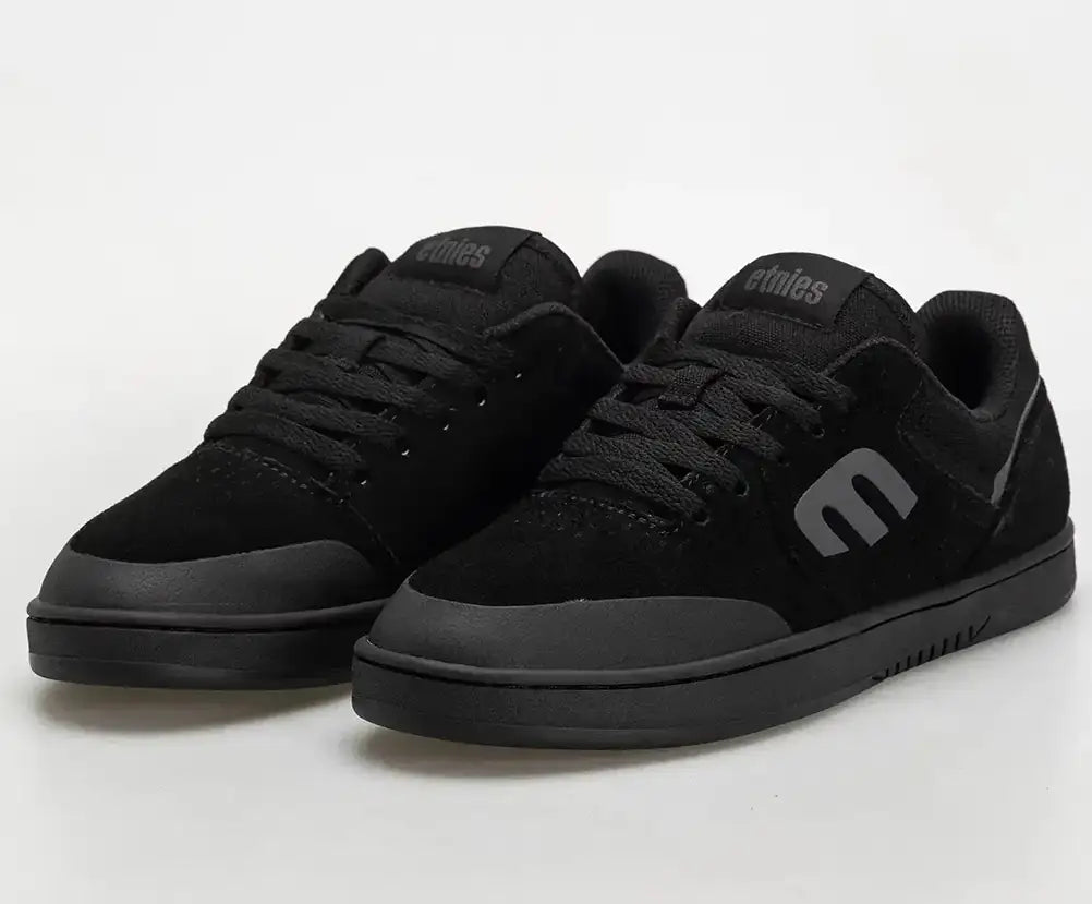 A pair of black low-top skate shoes with a matte finish, featuring a prominent stylized 'e' logo on the side and tongue, photographed on a light gray studio background.