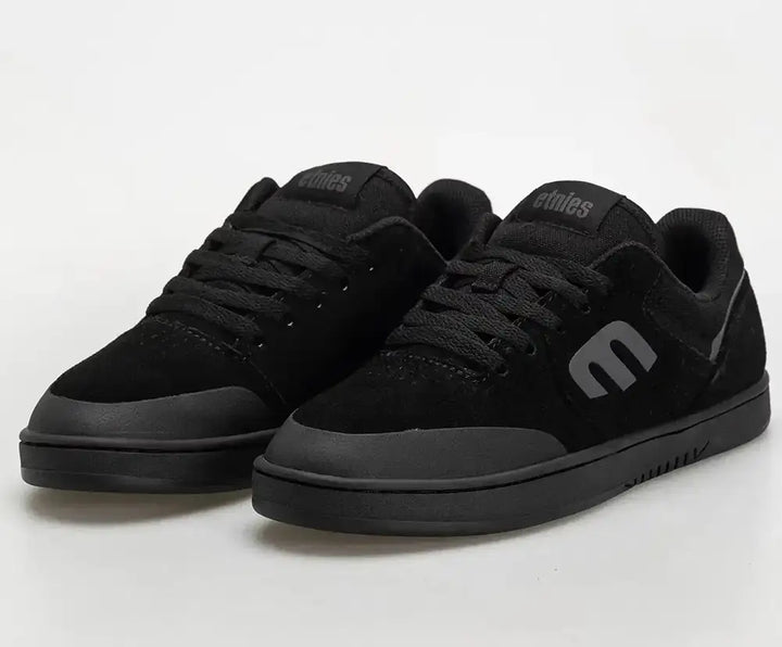 A pair of black low-top skate shoes with a matte finish, featuring a prominent stylized 'e' logo on the side and tongue, photographed on a light gray studio background.