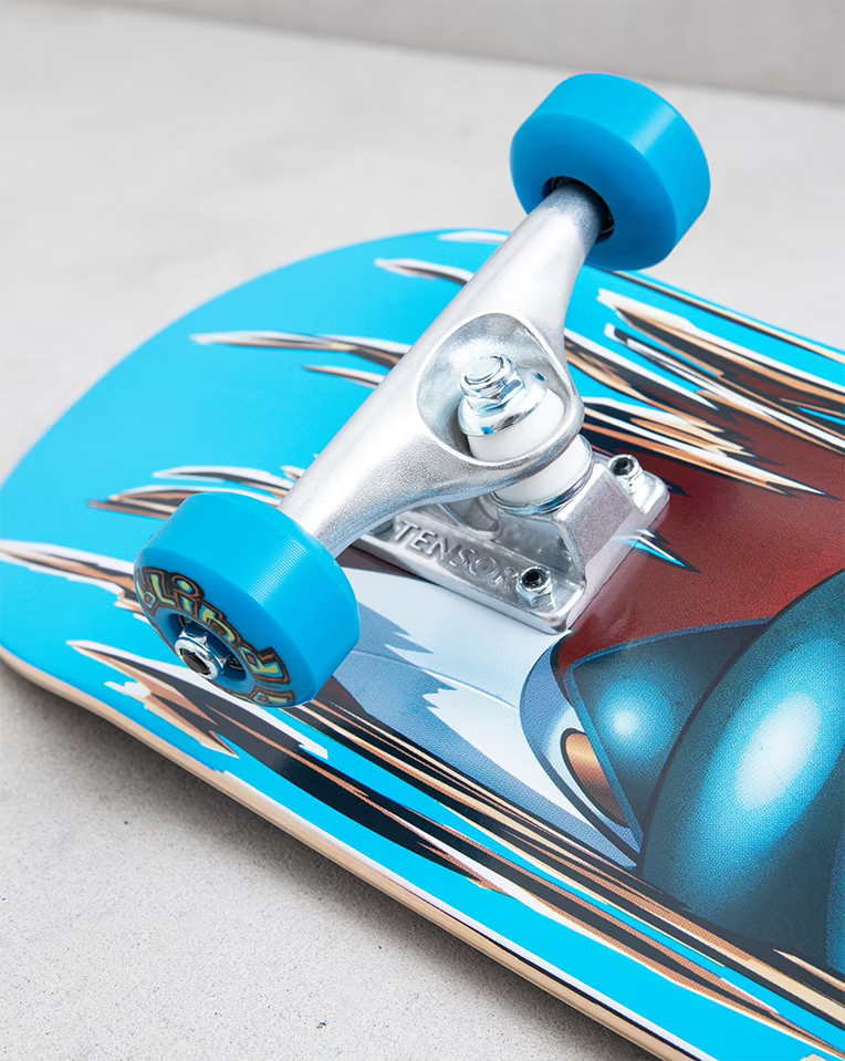Close-up of a skateboard deck with bright blue wheels and silver trucks on a light gray concrete surface. The deck features a glossy metallic blue and red graphic design with chrome-style streaks.