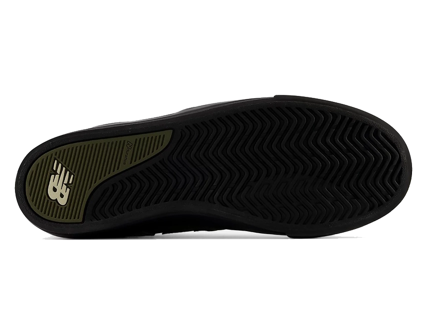 The outsole of a black sneaker, showing a textured black tread pattern and a green heel section with a white New Balance logo.
