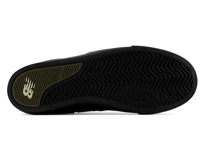 The outsole of a black sneaker, showing a textured black tread pattern and a green heel section with a white New Balance logo.
