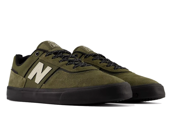 A pair of New Balance low-top skate shoes in olive green suede and mesh, featuring black laces, black soles, and a prominent cream-colored 'N' logo on the side.