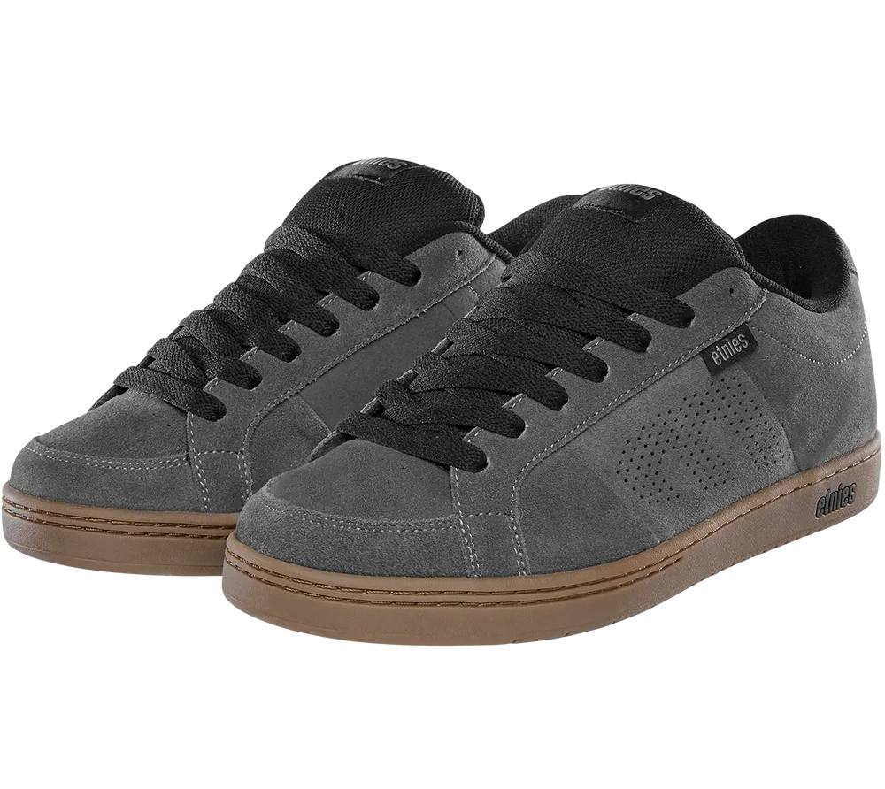 A pair of low-top skate shoes in dark gray suede with black laces, black tongue details, and a brown gum sole, shown against a plain white background.