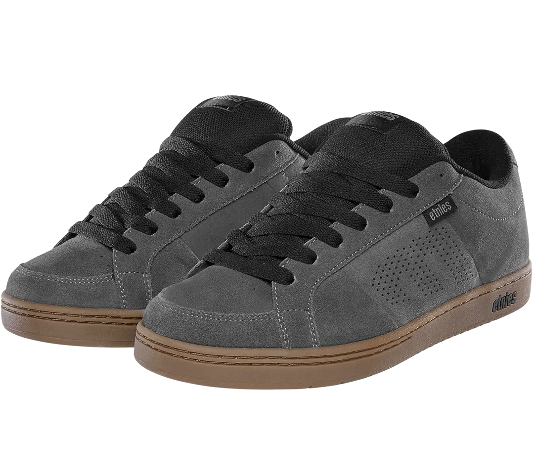 A pair of low-top skate shoes in dark gray suede with black laces, black tongue details, and a brown gum sole, shown against a plain white background.