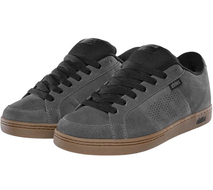 A pair of low-top skate shoes in dark gray suede with black laces, black tongue details, and a brown gum sole, shown against a plain white background.