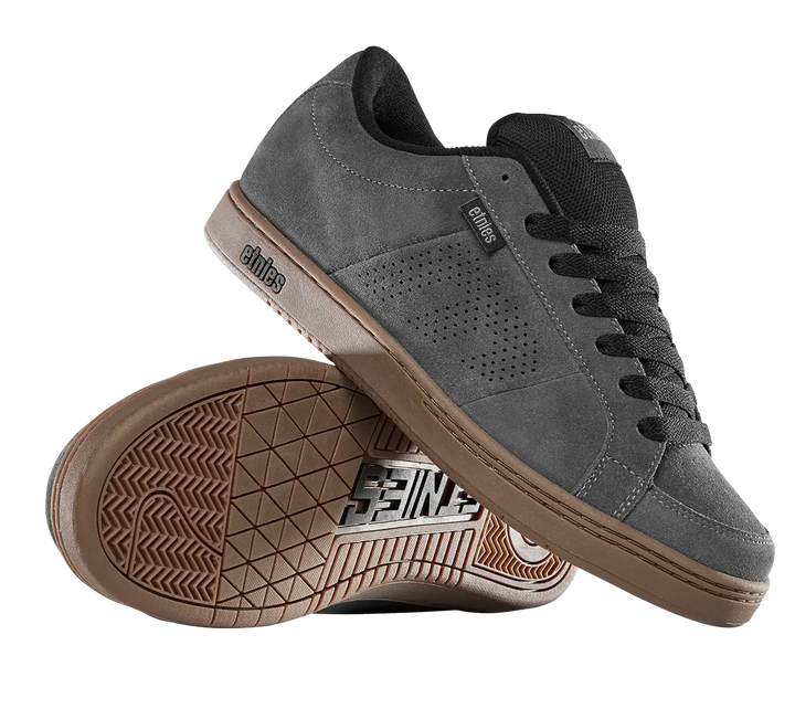 A pair of dark gray suede skate shoes with black laces and a brown gum sole, shown on a clean white background. One shoe is positioned upright while the other lies on its side to display the textured brown outsole.