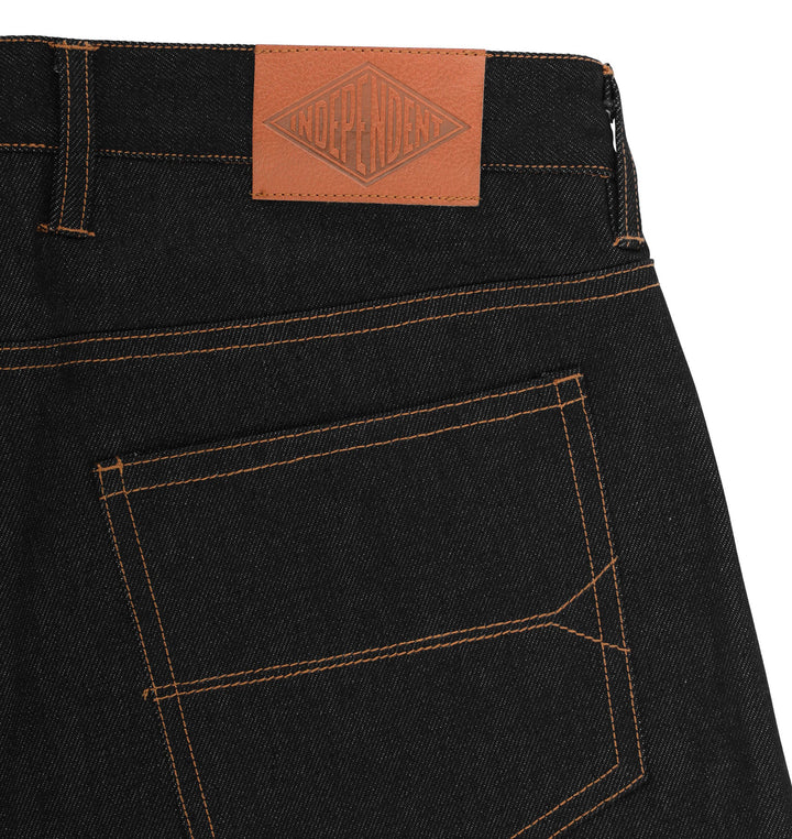 Close-up of the back waistband and pocket area of black denim jeans with orange contrast stitching and a tan leather patch at the waistband.