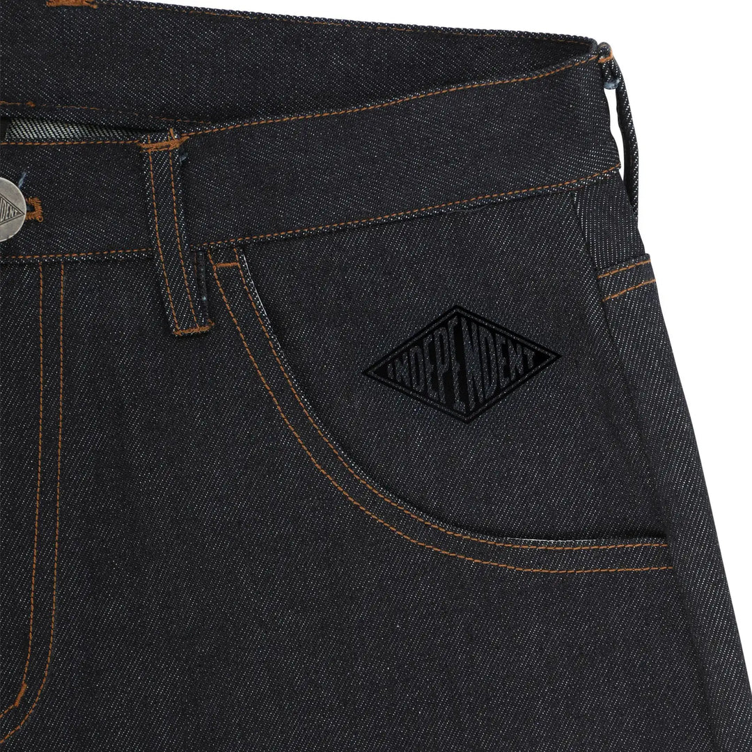 Close-up of dark indigo denim jeans showing the back pocket with a black embroidered diamond-shaped 'INDEPENDENT' logo patch and contrast orange stitching.