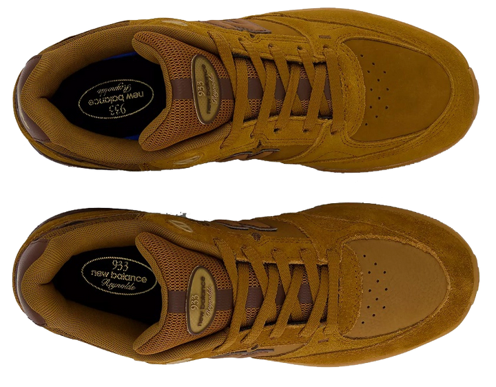 A pair of New Balance 935 sneakers in a monochromatic mustard brown colorway, shown from a top-down view on a solid white background.