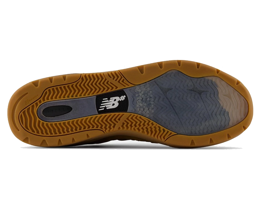 The outsole of a New Balance shoe, showing a brown gum rubber tread with a black and white New Balance logo and a translucent gray midsole section.