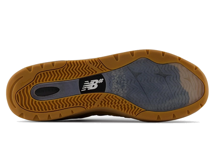 The outsole of a New Balance shoe, showing a brown gum rubber tread with a black and white New Balance logo and a translucent gray midsole section.