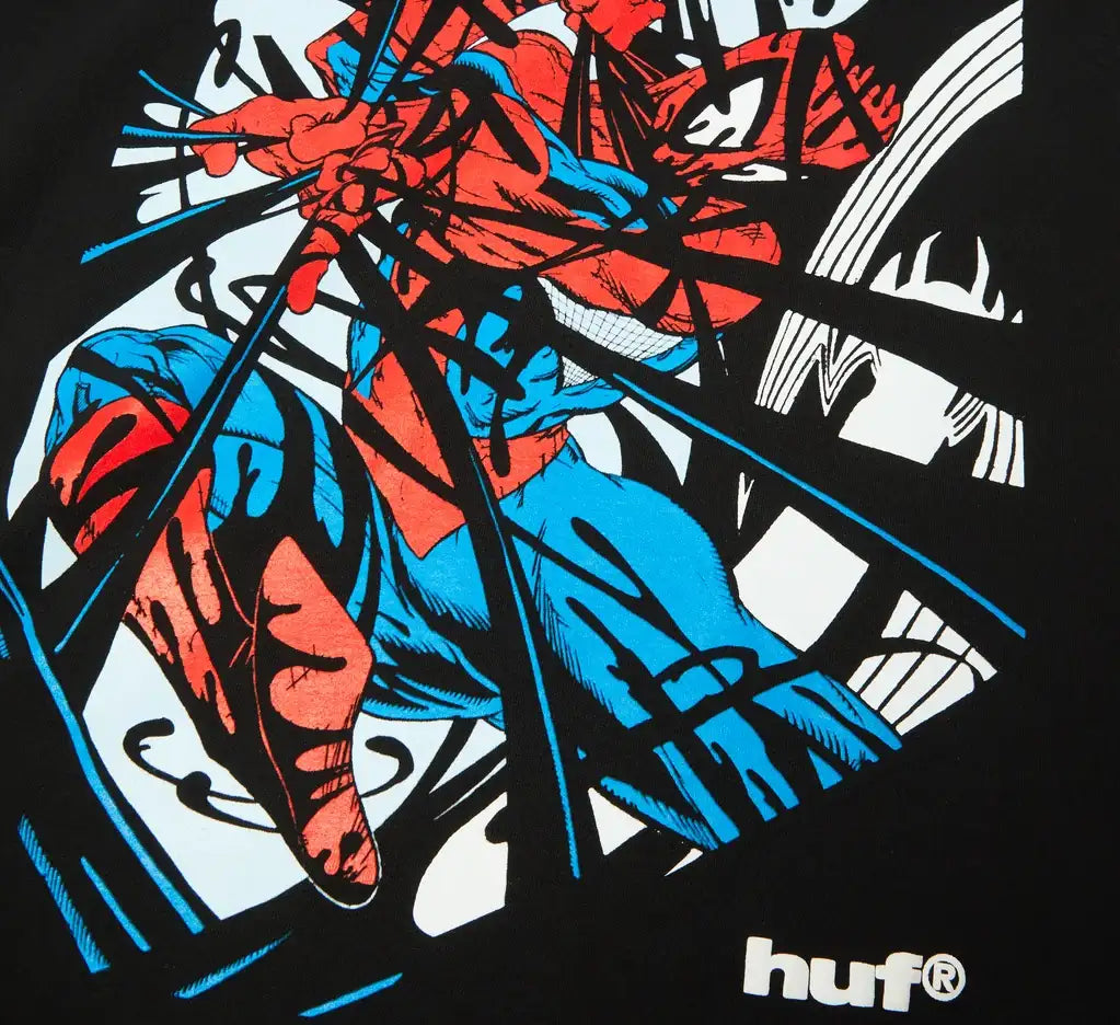 A close-up of a black graphic t-shirt featuring a stylized, comic-book style illustration of Spider-Man in red and blue, with blue speed lines and a white 'huf®' logo on the bottom right.