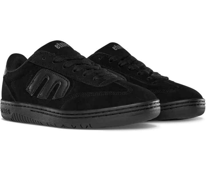 A pair of black low-top skate shoes from Elixir, featuring a suede and leather mix, tonal black logo detailing, and black laces, shown against a plain white background.