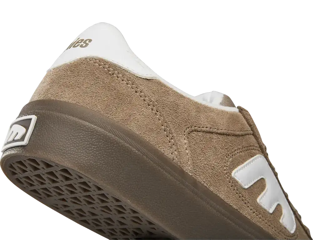 A close-up shot of a New Balance sneaker showing the side profile, featuring a brown suede upper, a white heel tab with gold branding, a white side logo, and a brown rubber sole.