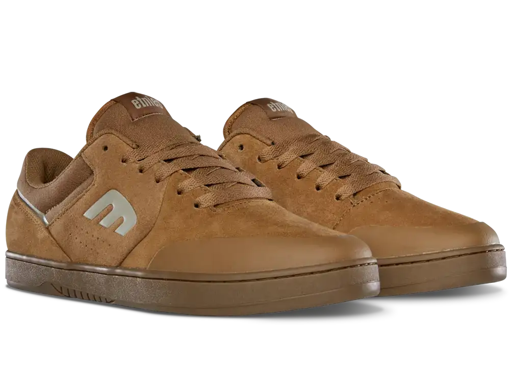 A pair of low-top skate shoes in a warm brown suede and leather mix, featuring a metallic silver 'm' logo on the side, brown laces, and a matching brown rubber sole, shown against a plain white background.