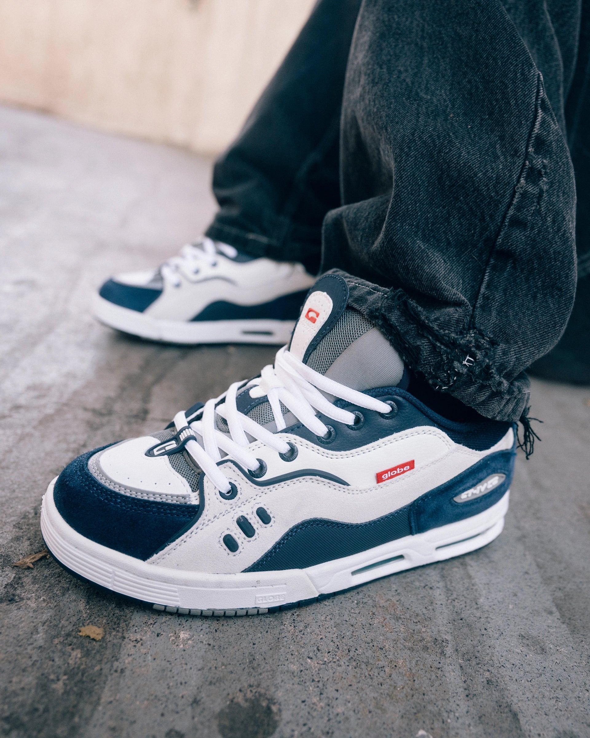 Close-up of Globe CT-IV White Navy skate shoes on feet, showing suede overlays, red logo tag, and 2000s skate style