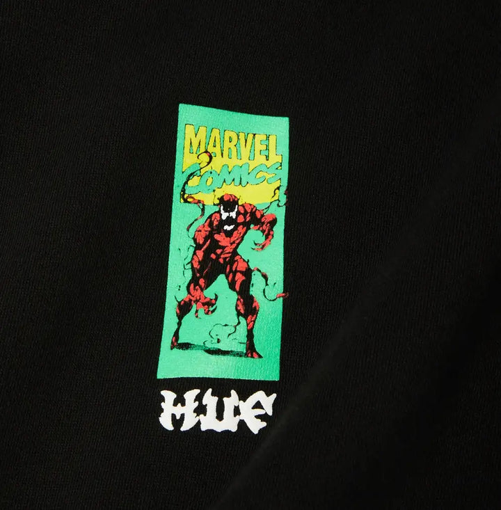 A close-up of a black garment featuring a vertical green graphic with a red Marvel Comics character and yellow 'MARVEL COMICS' text, plus a white stylized 'HUE' logo below.