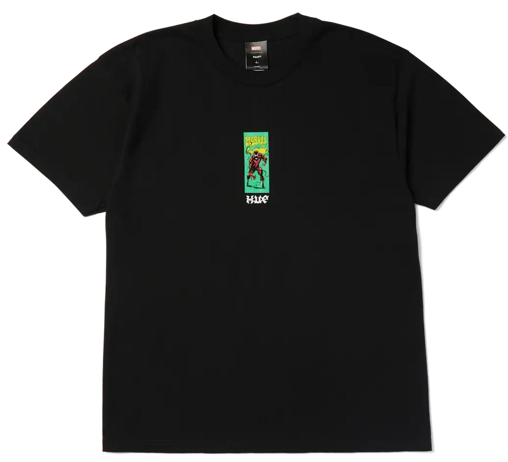 A black short-sleeve crewneck t-shirt featuring a small graphic print on the left chest. The graphic depicts a character in a red outfit against a green background with yellow text, and the word 'HUGO' printed in white below.