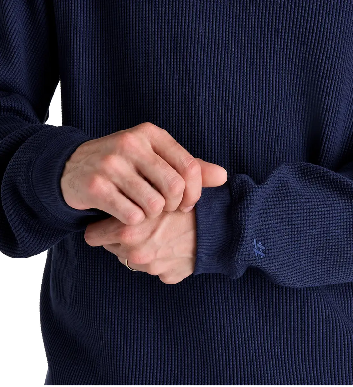 Close-up of a person wearing a navy blue waffle-knit sweater, showing the textured fabric and ribbed cuffs with hands clasped together.