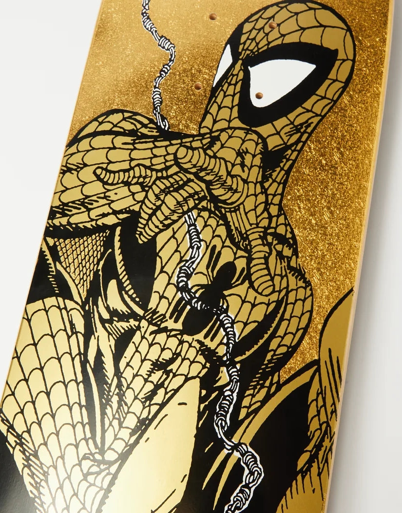 A close-up of a skateboard deck featuring a comic-style illustration of Spider-Man in black and gold, with a glittery gold background and white eye details.