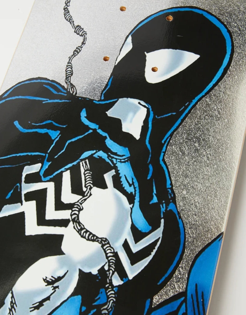 Close-up of a skateboard deck featuring a comic-style black and blue spider character with white eye and chest details on a silver textured background.