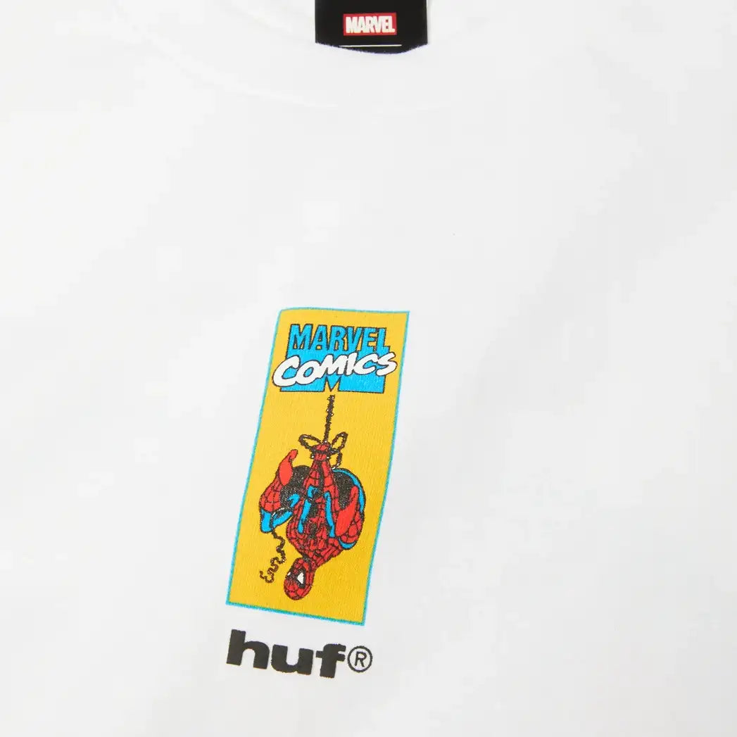 White crewneck t-shirt featuring a yellow and blue 'Marvel Comics' Spider-Man graphic on the chest, with a black Marvel brand tag at the collar and a black 'huf' logo printed below the graphic.