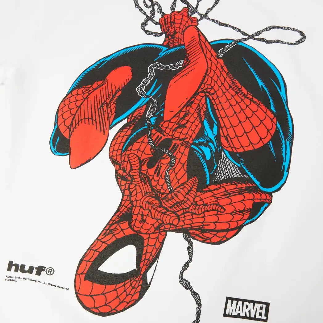 A close-up of a white graphic print featuring Spider-Man hanging upside down, with the HUF logo on the bottom left and the Marvel logo on the bottom right.