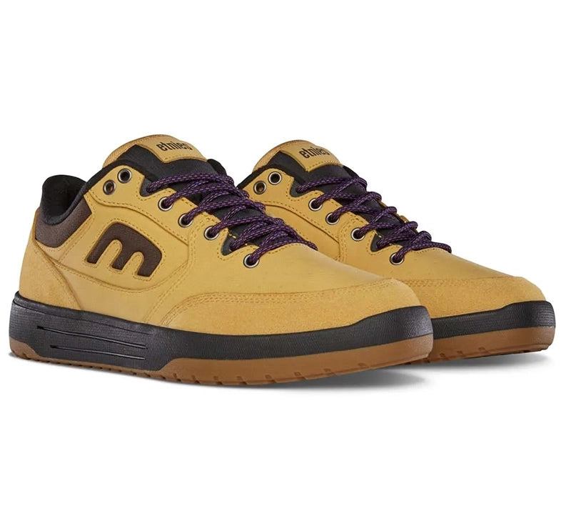 A pair of M Mutual low-top sneakers in mustard yellow with dark brown and purple accents, featuring dark brown laces and a black and brown sole, set against a plain white background.