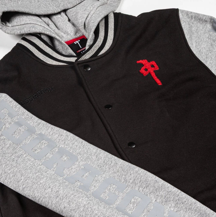A close-up of a varsity-style hooded jacket with a black body, gray sleeves and hood, striped ribbed collar, snap front, and a red embroidered logo on the chest.