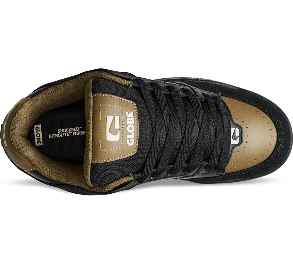 A top-down view of a Globe Shocked athletic shoe in black and metallic gold, showing the tongue, laces, and toe cap on a white background.